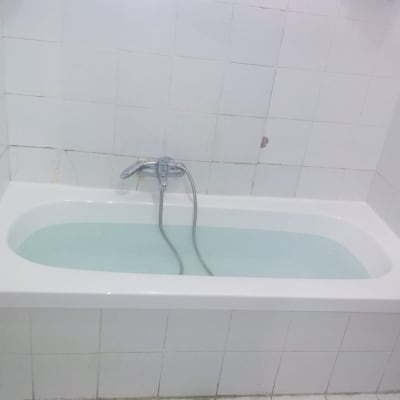 אמבטיה עם מים וברז מתכת על קיר מרוצף