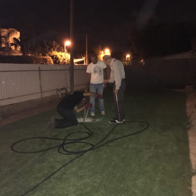 שלושה אנשים עובדים עם צינור בגינה בלילה