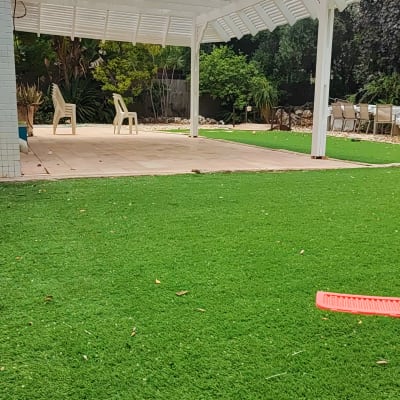 דשא סינתטי ירוק עם פרגולה לבנה וכיסאות פלסטיק.