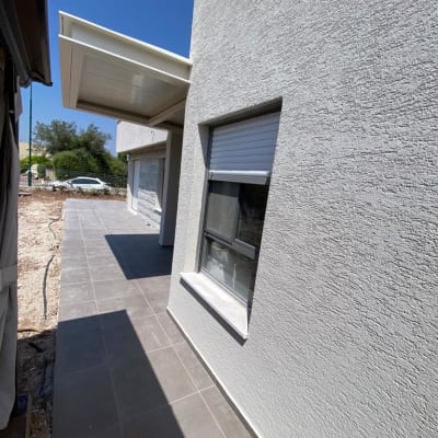 קיר חיצוני עם חלון ותריס סגור, שביל מרוצף