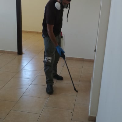 אדם עם מסכה מרסס חומר הדברה על הרצפה