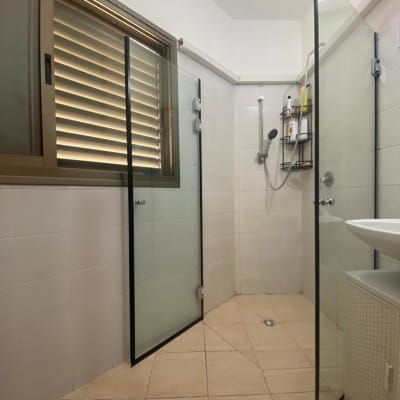 מקלחון עם דלתות זכוכית ומדף עם מוצרי רחצה