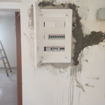 לוח חשמל פתוח על קיר עם תיקוני טיח