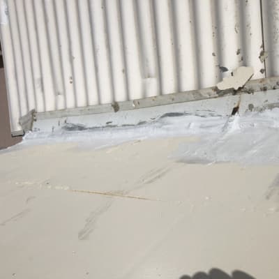 איטום גג עם חומר לבן ליד קיר מתכת