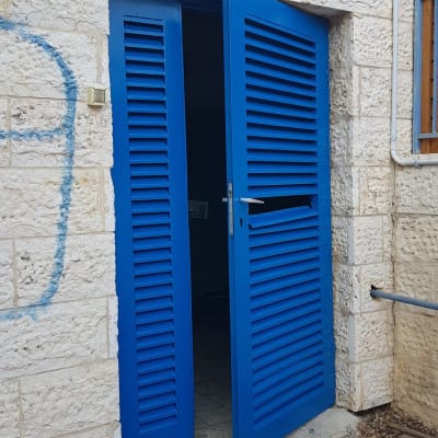 דלתות תריס כחולות פתוחות בקיר אבן