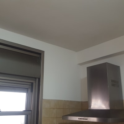 קיר צבוע בלבן ליד חלון ומנדף מתכת