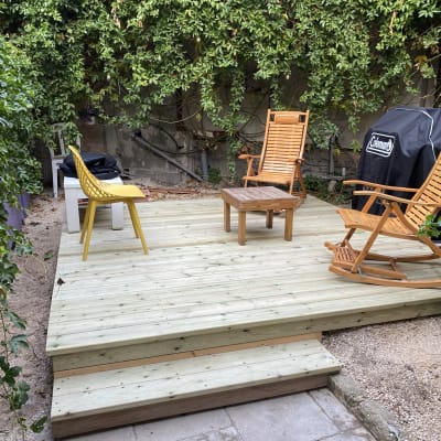 דק עץ עם כיסאות נדנדה ושולחן קטן בגינה