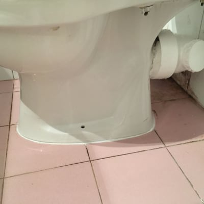 אסלה עם חיבורי צנרת על רצפת קרמיקה ורודה