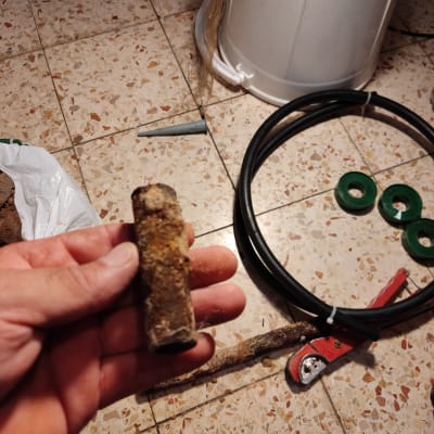 יד מחזיקה צינור חלוד, כלי עבודה וצינור פלסטיק על הרצפה