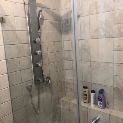 מקלחת עם ראש מקלחת, בקבוקי שמפו ומרכך על מדף