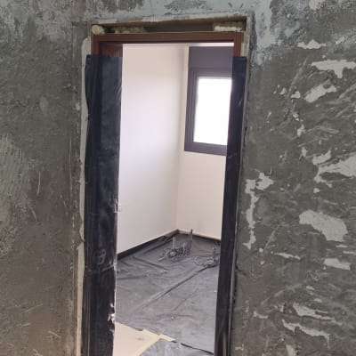 חדר בשיפוץ עם קירות חשופים, שקיות פסולת ורצפה מכוסה בניילון