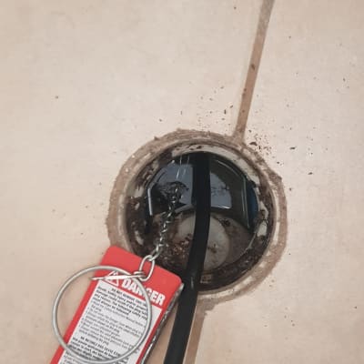 כבל שחור עם תג אזהרה אדום בתוך פתח ניקוז