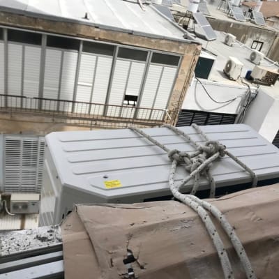 יחידת מזגן חיצונית קשורה בחבלים על גג בניין