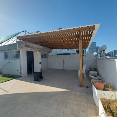 פרגולה מעץ על גג עם עציצים וכיסאות פלסטיק