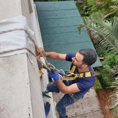 אדם עם כפפות כחולות מבצע איטום על קיר חיצוני