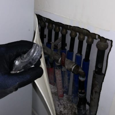 צנרת מים בקיר עם יד אוחזת בכלי עבודה