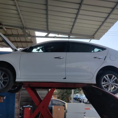 רכב לבן על מעלית במוסך עם מכסה מנוע פתוח