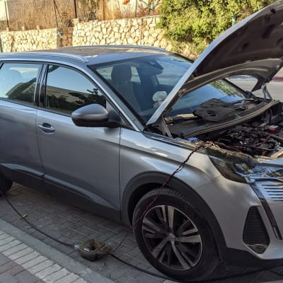 אדם מתקן רכב עם מכסה מנוע פתוח וכבלים מחוברים