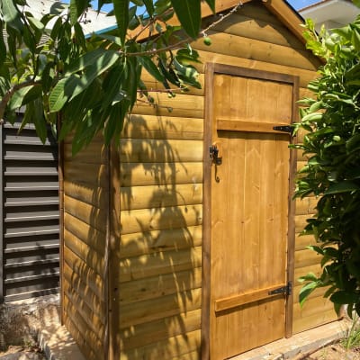 מחסן עץ בגינה עם דלת סגורה וצל עלים