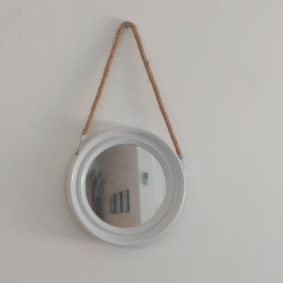 מראה עגולה תלויה על חבל על קיר לבן