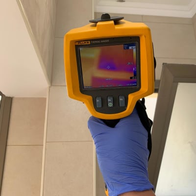 מד חום תרמי צהוב מוחזק ביד עם כפפה כחולה