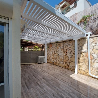 פרגולה לבנה מעץ בחצר מרוצפת אבן