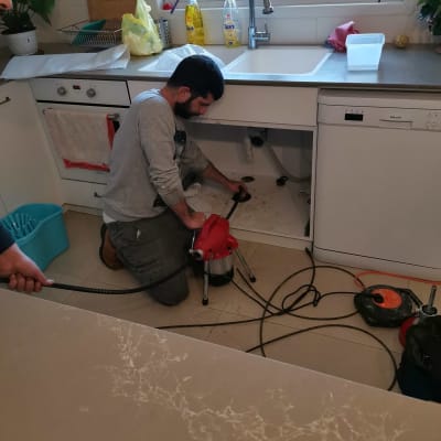 אדם מתקן צנרת מתחת לכיור במטבח