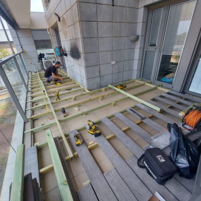 אדם עובד על בניית דק מעץ במרפסת עם כלים חשמליים.