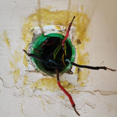 חוטי חשמל חשופים יוצאים מקופסת חיבורים בקיר