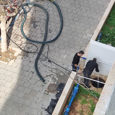 שני אנשים עובדים עם צינור ליד פתח ביוב