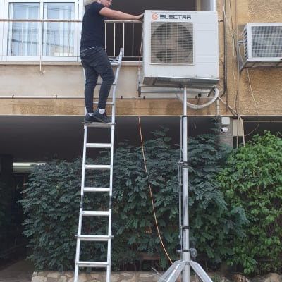 אדם על סולם מתקין מזגן על קיר חיצוני