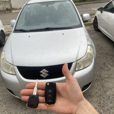 מפתח ושלט לרכב מוחזקים מול רכב סוזוקי כסוף