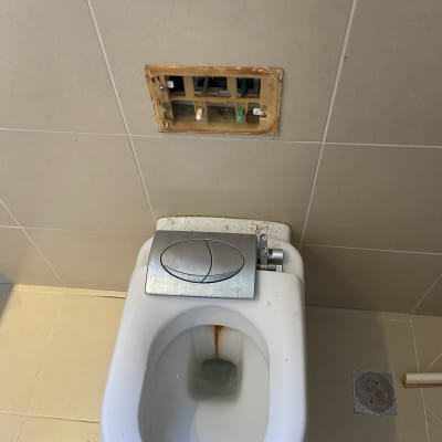 אסלה עם לחצן הדחה, קיר פתוח עם צנרת חשופה