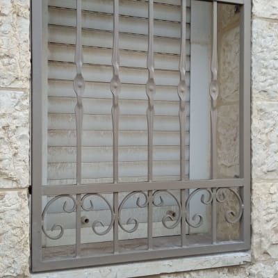 סורג מתכת מעוצב על חלון עם תריסים