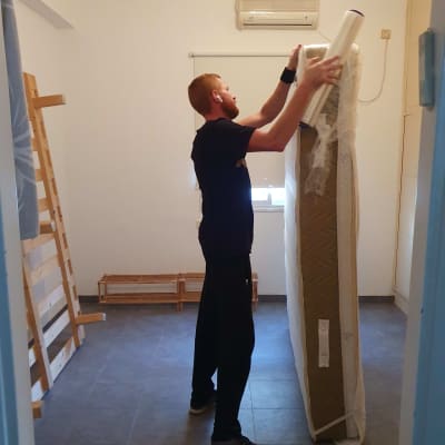 אדם עוטף מזרן בניילון בחדר ריק