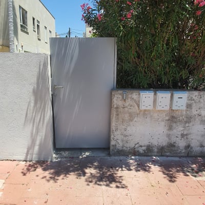 שער מתכת אפור ליד תיבות דואר על קיר בטון