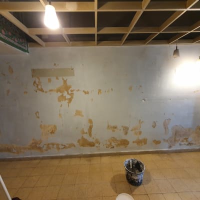 קיר עם קילופי צבע ודלי צבע על הרצפה