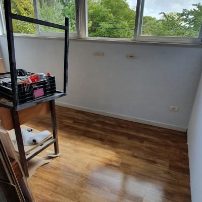 חדר עם רצפת עץ, מדף עם מוצרי ניקוי ונייר מגבת.