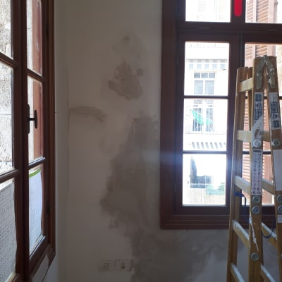 קיר עם תיקוני טיח וסולם עץ ליד חלון