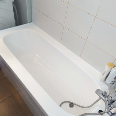 אמבטיה לבנה עם ברז מתכת וקיר אריחים לבנים