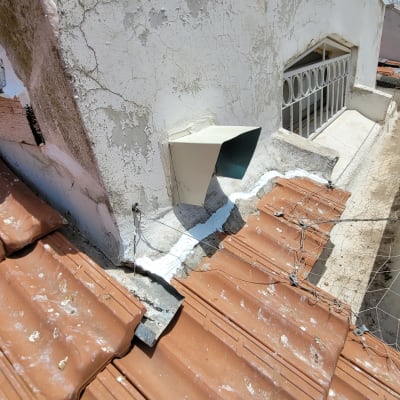 רעפים חומים על גג עם צינור אוורור וקיר לבן מתקלף