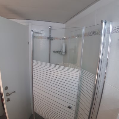 מקלחון עם דלת זכוכית ומדף למוצרי רחצה