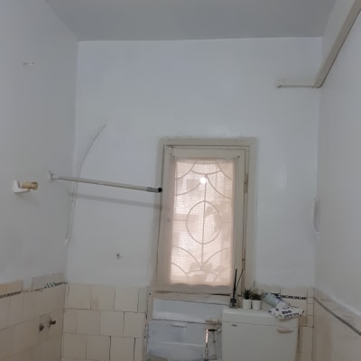 קיר אמבטיה עם אריחים לבנים, חלון קטן, צינור תלוי