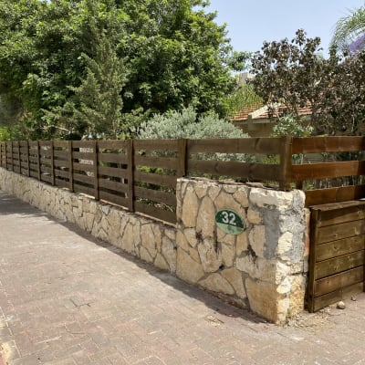גדר עץ חומה על קיר אבן בגינה