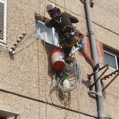 אדם עם קסדה עובד בגובה על קיר בניין