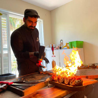 שף משתמש במבער להכנת מנות עם להבות על שולחן עץ