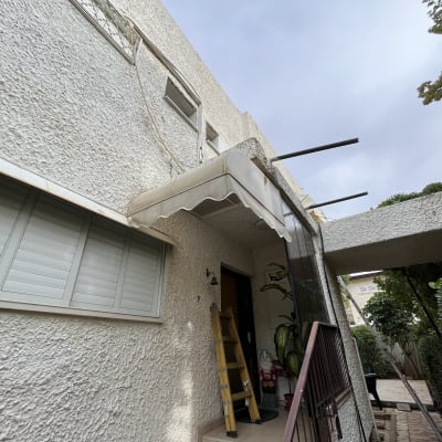 סוכך לבן מותקן מעל כניסה לבית עם תומכות מתכת.