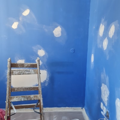 קיר כחול עם תיקוני צבע, סולם ודלי צבע