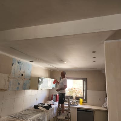 אדם עומד על סולם ומורח גבס על התקרה