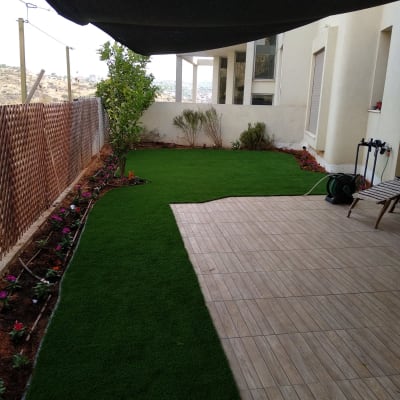 גינה עם דשא סינתטי, צמחים ופרחים לאורך הגדר